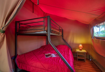 Vista interna della tenda safari Freeflower Confort con letto a castello e tavolino a Flower Camping La Sagne.
