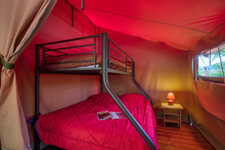 Vista interna della tenda safari Freeflower Confort con letto a castello e tavolino a Flower Camping La Sagne.