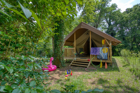 Außenansicht eines Wood Lodge Confort Safari-Zeltes, umgeben von Natur, mit Spielzeug und Paddeln davor.