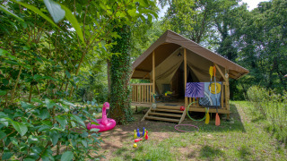 Außenansicht eines Wood Lodge Confort Safari-Zeltes, umgeben von Natur, mit Spielzeug und Paddeln davor.