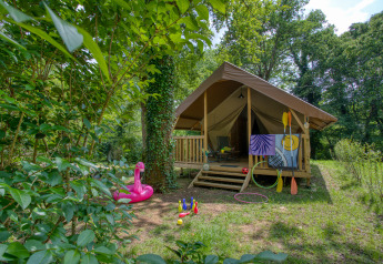 Udendørs billede af et Wood Lodge Confort safari telt omgivet af natur, med legetøj og kajakårer foran.