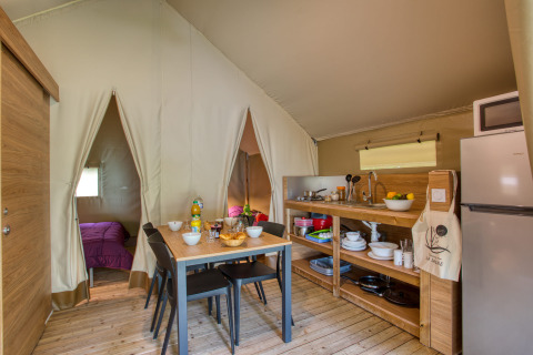 Binnenkant van een safaritent met keuken, eettafel en slaapkamer bij Flower Camping La Sagne in Frankrijk.
