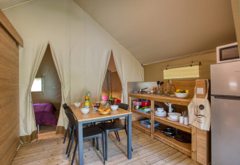Indvendigt billede af et safari telt med køkken, spisebord og soveværelse hos Flower Camping La Sagne.