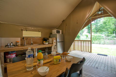 Binnenzicht van een safaritent met keuken en eettafel in Wood Lodge Confort, Flower Camping La Sagne.