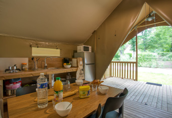Indvendig udsigt af et safari-telt med køkken og spisebord på Wood Lodge Confort, Flower Camping La Sagne.