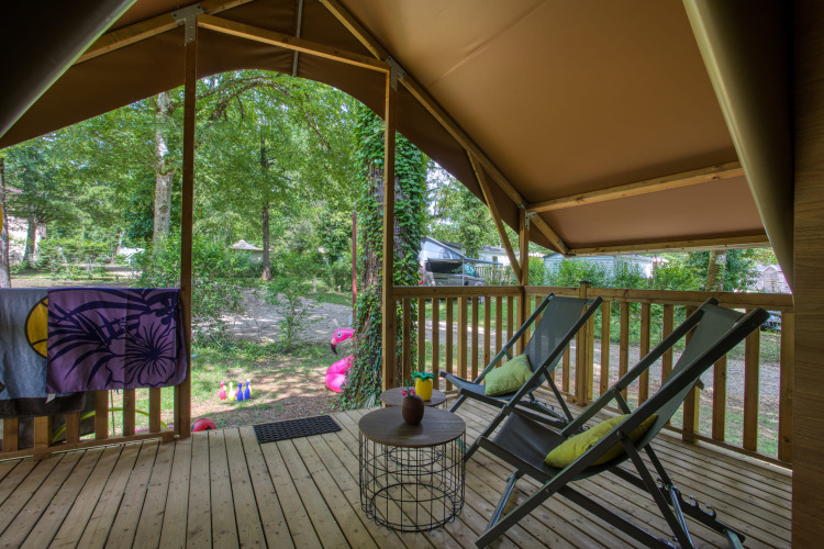 View from a safari tent deck with two lounge chairs and a table at Flower Camping La Sagne, France.