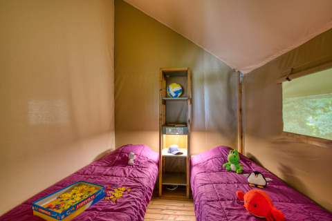 Binnenkant van de Wood Lodge Confort safaritent op Flower Camping La Sagne, Frankrijk, met twee bedden en speelgoed.