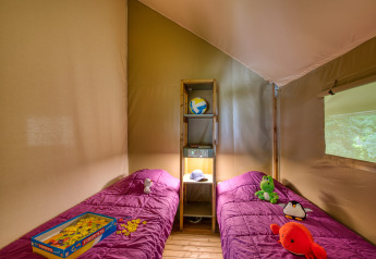 Interno della tenda safari Wood Lodge Confort al Flower Camping La Sagne, Francia, con due letti e giocattoli.