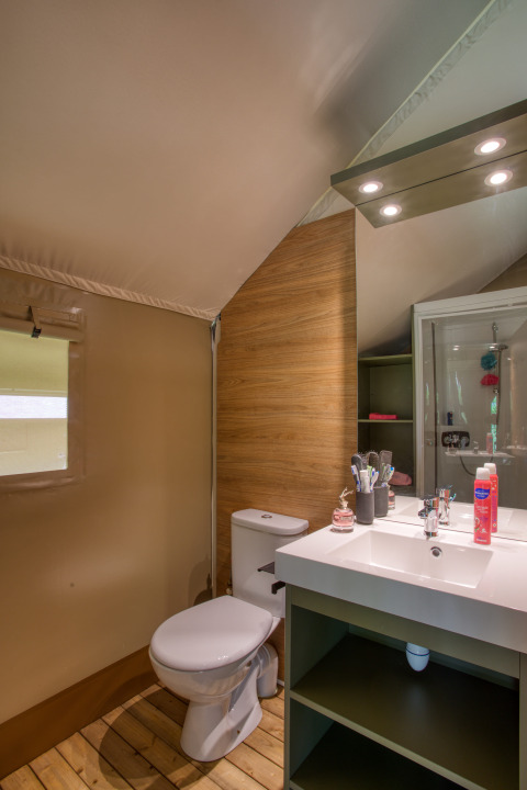 Badkamer in safaritent Wood Lodge Confort op Flower Camping La Sagne, met toilet en wastafel.