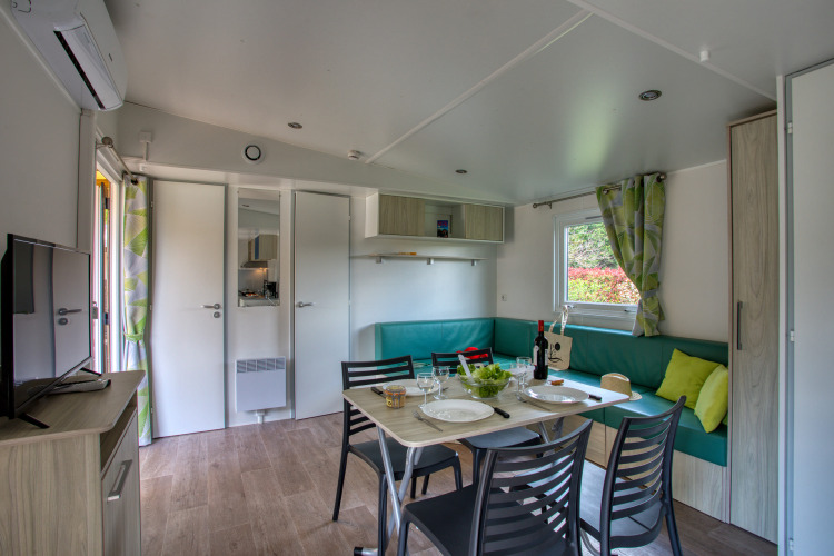 Interno del lodge Stacaravan Campbell Premium presso Flower Camping La Sagne in Francia, zona pranzo e divano.