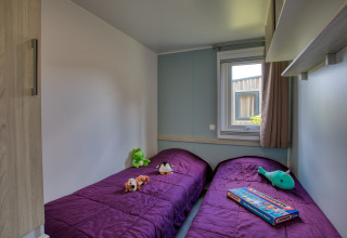 Deux lits simples avec couettes violettes, jouets et fenêtre dans le lodge Stacaravan Campbell Premium en France.