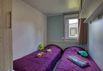 Due letti singoli con coperte viola, giochi e una finestra al Stacaravan Campbell Premium in Francia.