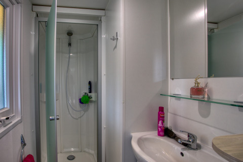 Salle de bains moderne avec cabine de douche, lavabo et miroir au Stacaravan Campbell Premium, La Sagne.