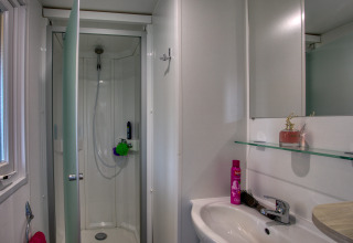 Salle de bains moderne avec cabine de douche, lavabo et miroir au Stacaravan Campbell Premium, La Sagne.