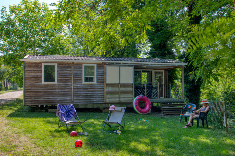 Casa mobile Stacaravan Cayuga Confort in legno, con sedie da giardino, giocattoli e verde circostante.