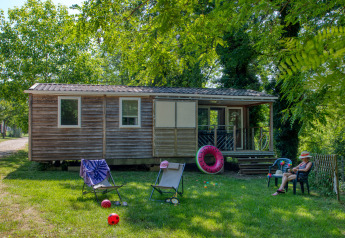 Casa mobile Stacaravan Cayuga Confort in legno, con sedie da giardino, giocattoli e verde circostante.