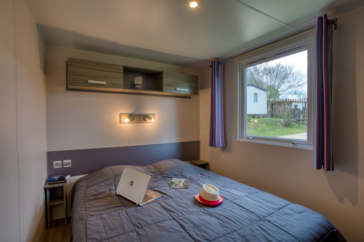 Slaapkamer in Stacaravan Cayuga Confort bij Flower Camping La Sagne in Frankrijk met raam en uitzicht.