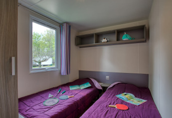 To enkeltsenge med lilla sengetæpper i et mobilhome på Flower Camping La Sagne, Stacaravan Cayuga Confort.