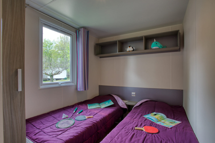 Twee eenpersoonsbedden met paarse dekbedden in een stacaravan op Flower Camping La Sagne, Stacaravan Cayuga Confort.