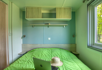 Camera da letto moderna con coperta verde, cappello e laptop HP presso Stacaravan Arlequin Premium in Francia.