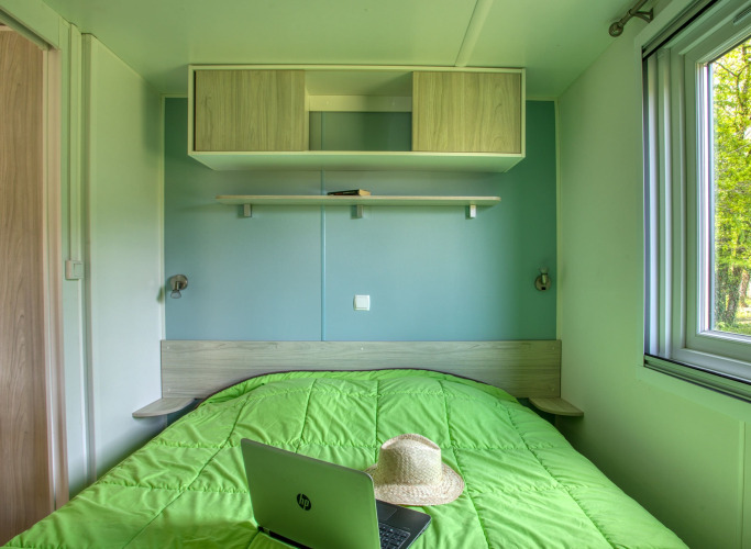 Slaapkamer met groen dekbed, hoed en HP-laptop in de Stacaravan Arlequin Premium bij Flower Camping La Sagne.