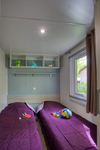 Chambre confortable au Stacaravan Arlequin Premium, Flower Camping La Sagne, avec deux lits et des jouets.
