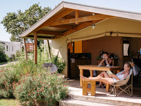 Two people relax at a wooden table and chair under the canopy at a Ecolodge Cotton Toilée CONFORT safari tent.
