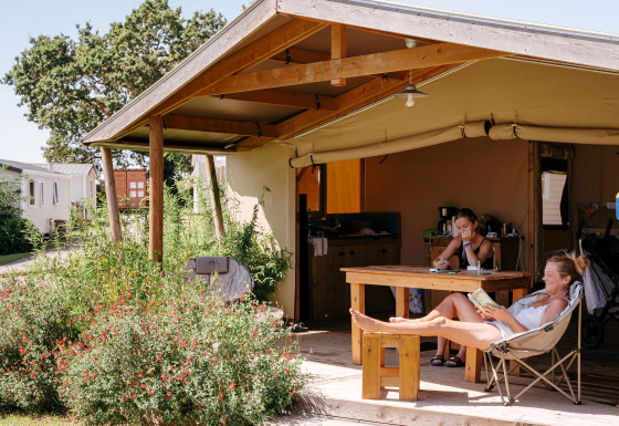 Two people relax at a wooden table and chair under the canopy at a Ecolodge Cotton Toilée CONFORT safari tent.
