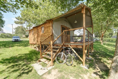 Hut Lodge CONFORT cabin with wooden porch, bicycles, and lush greenery surrounding it on a sunny day.
