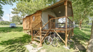 Hut Lodge CONFORT cabin with wooden porch, bicycles, and lush greenery surrounding it on a sunny day.