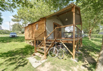 Hytte Lodge CONFORT med træterrasse, cykler og grønne omgivelser, set udefra på en solskinsdag.