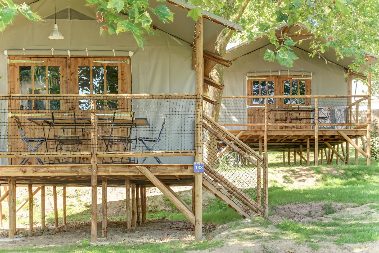 Verhoogde houten hutten met netterrassen tussen bomen bij Flower Camping Le Conleau in Frankrijk.