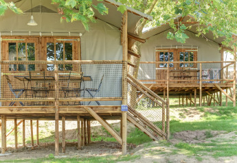 Zwei erhöhte Kabinen mit Holzveranden und Netzzaun im Grünen bei Flower Camping Le Conleau, Frankreich.