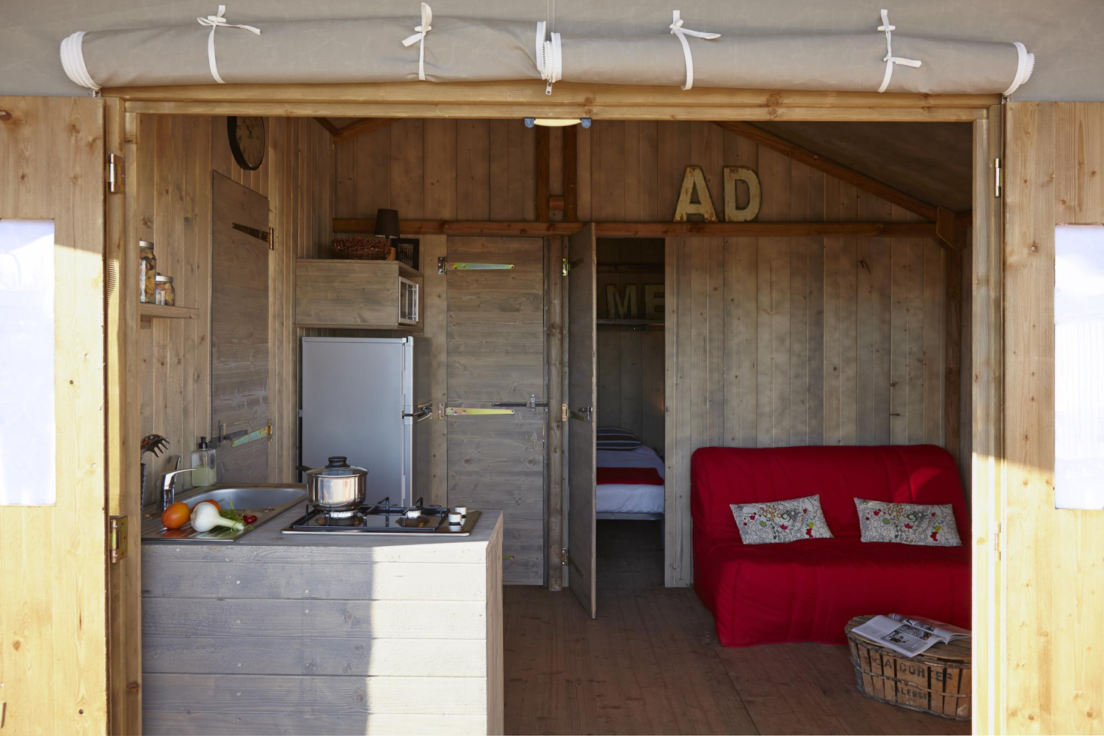 Binnenaanzicht van een knusse houten lodge met kitchenette, bank en slaapkamer in Hut Lodge CONFORT, Frankrijk.