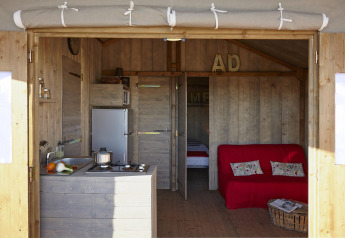 Interieur van een gezellige houten lodge met keukenhoek, sofa en slaapruimte bij Hut Lodge CONFORT, Frankrijk.