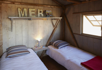 Deux lits simples dans un hébergement glamping chaleureux avec murs en bois et lumière naturelle de la fenêtre.