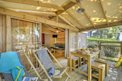 Sunny wooden deck with lounge chairs and dining table at Hut Lodge Cosyflower PREMIUM, Flower Camping Le Conleau.