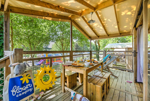 Wooden terrace at Hut lodge Cosyflower PREMIUM, breakfast set on table, toys and trees, Le Conleau, France.