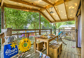 Terrasse der Hut lodge Cosyflower PREMIUM mit Frühstückstisch, Spielzeug und Waldblick auf Campingplatz.