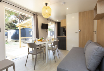 Moderne glamping-indkvartering med lys stue, spiseplads, køkken, sofa og udsigt til terrassen.