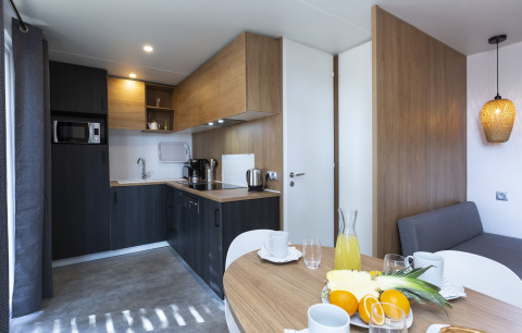Cocina moderna de glamping con mesa, frutas frescas, cafetera y acabados de madera luminosa.