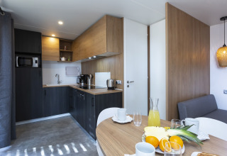 Modern glamping kitchen with dining table, fresh fruit, coffee maker, and bright wood finishes.