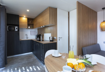 Modern glamping kitchen with dining table, fresh fruit, coffee maker, and bright wood finishes.
