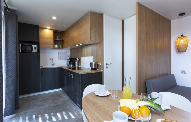 Modernes Glamping-Küchenbereich mit Esstisch, frischem Obst und stilvollem Interieur in hellem Holz.