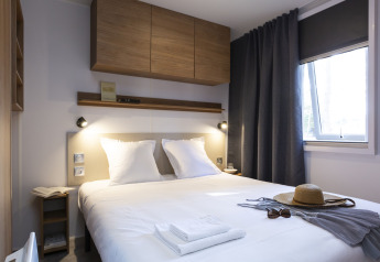 Hébergement glamping moderne avec lit double confortable, décoration chaleureuse et lumière naturelle.