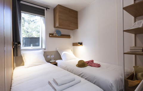 Alloggio glamping moderno con due letti singoli, luce naturale dalla finestra e mobili in legno.