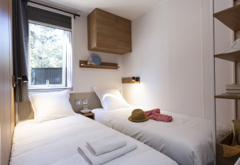 Alloggio glamping moderno con due letti singoli, luce naturale dalla finestra e mobili in legno.