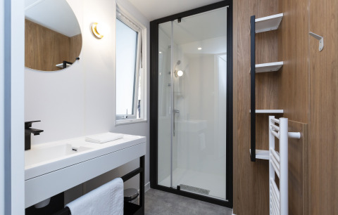 Modern bathroom in glamping accommodation with glass shower, white sink, wood panel walls and towel rack.