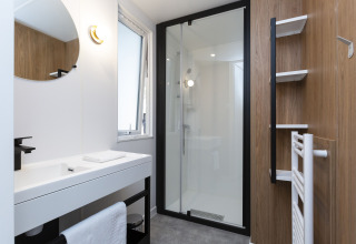Modernes Badezimmer in einer Glamping-Unterkunft mit Dusche, weißem Waschbecken und Holzverkleidung.