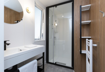 Bagno moderno in una sistemazione glamping con doccia a vetro, lavabo bianco e pareti in legno.